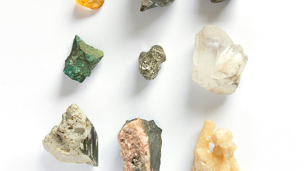 Assortment of rough, uncut gemstones in different colors arranged on a white surface