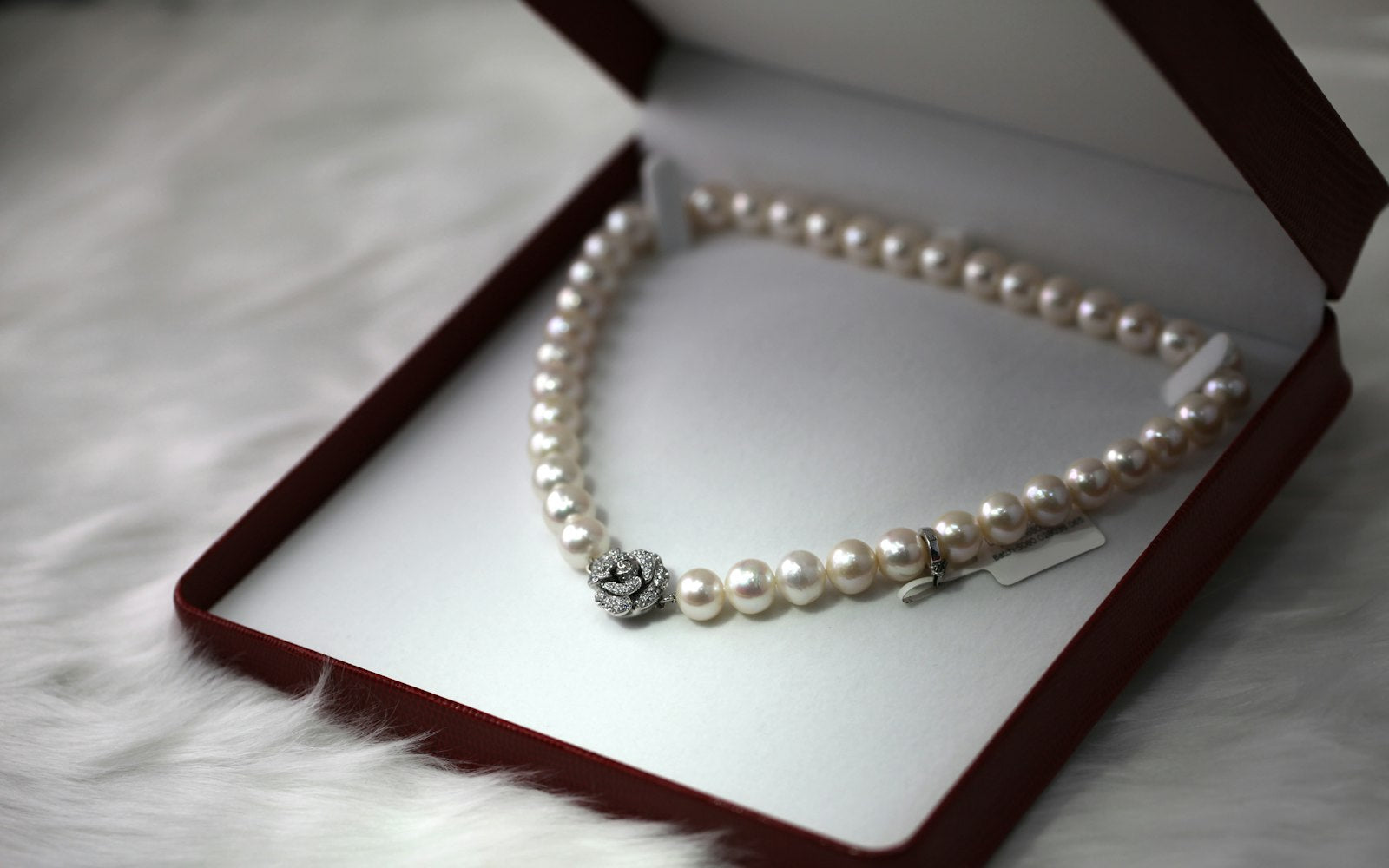 Pearl strand necklace with a pavé flower clasp in an open red jewelry box